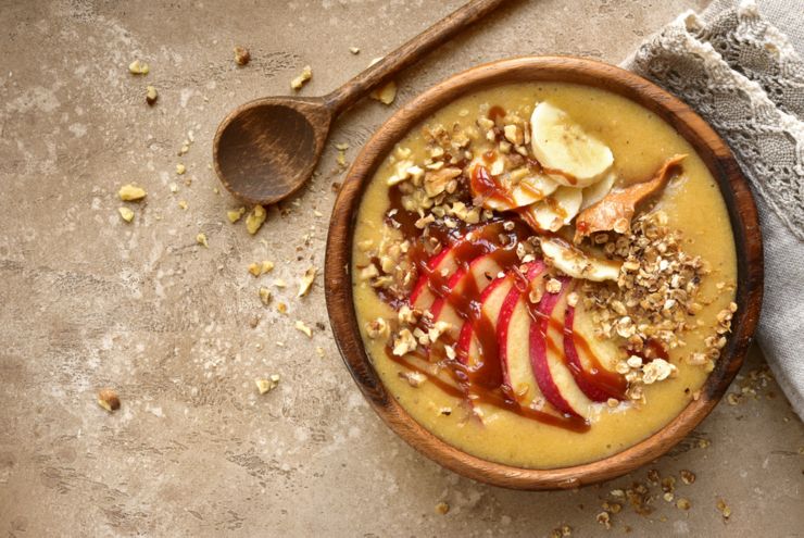 Bowl of apple banana smoothie with granola, caramel and peanut butter (apple pie) over beige or sand slate, stone or concrete background.Top view with copy space.