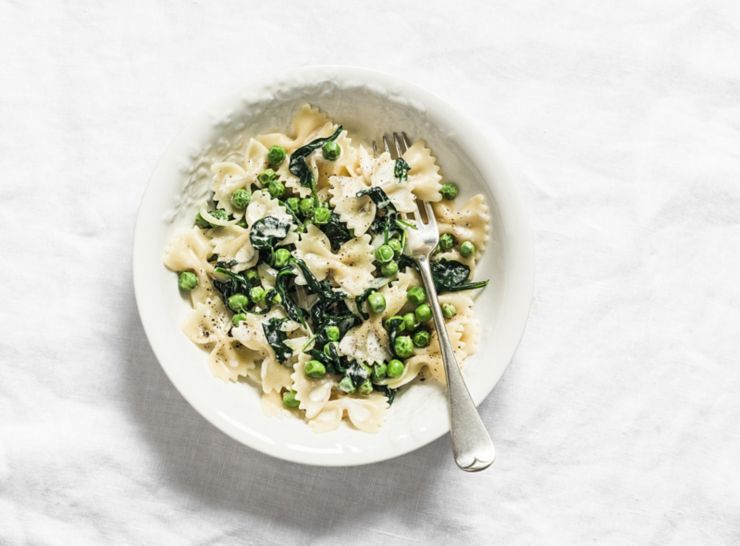 Farfalle pasta with green peas spinach cream sauce on light background, top view