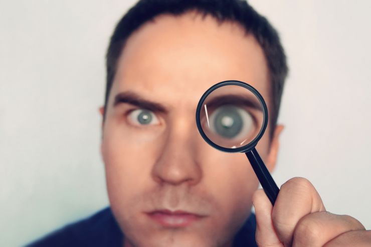 Man on white background curiously looks through the magnifying glass. Male fuzzy eye magnified through the loule. Person uses magnifier to look closely at some object. Detective search for evidence