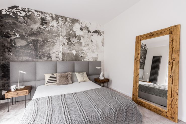 Grey king-size bed in a spacious bedroom with an abstract wallpaper on the wall and a large wood framed mirror