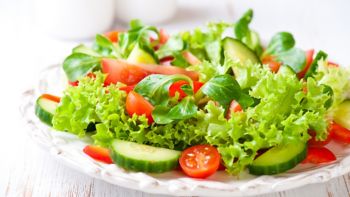 Tasty salad with different tomatoes, red pepper, lambs lettuce, cucumber, lettuce and lambs lettuce. Summer salad. Healthy snack. Concept for a tasty and healthy meal. White wooden background Close up
