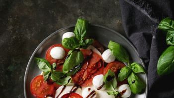 Italian caprese salad with sliced tomatoes, mozzarella cheese, basil, olive oil. Served in vintage metal plate on textile napkin over dark metal background. Top view. Rustic style. Square image