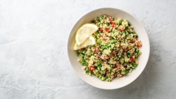 Traditional Arabic Salad Tabbouleh with couscous, vegetables and greens on concrete background. Top view. Copy space.