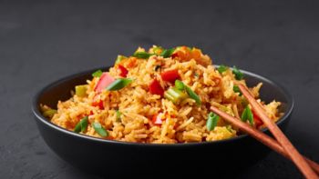 Veg Schezwan Fried Rice in black bowl at dark slate background. Vegetarian Szechuan Rice is indo-chinese cuisine dish with bell peppers, green beans, carrot. Copy space