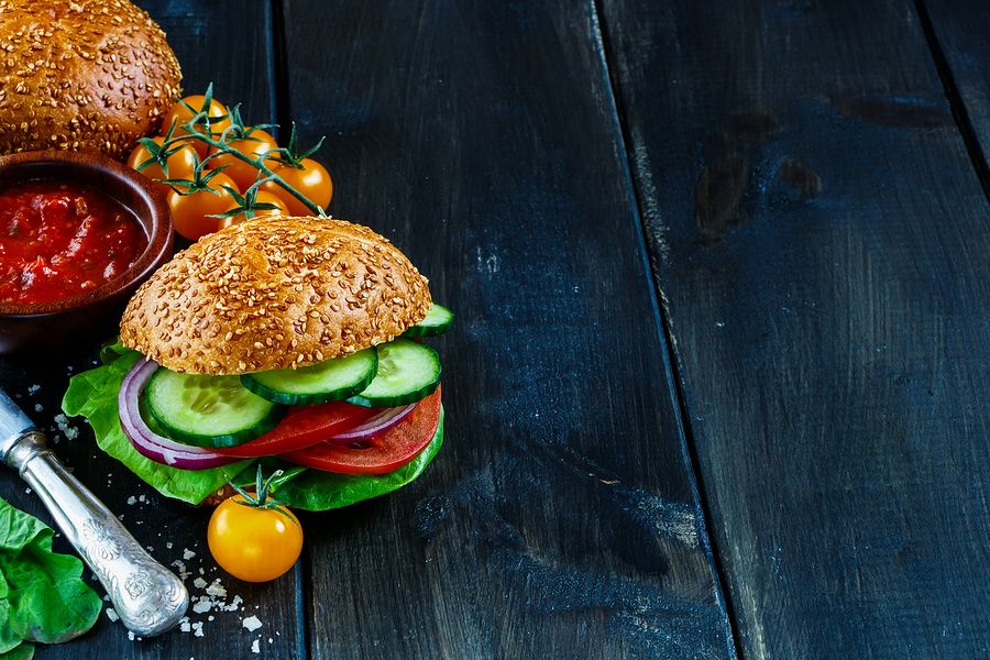 Freshly made vegan burger with vegetables on dark rustic wooden table selective focus border. Healthy fast food background with space for text.