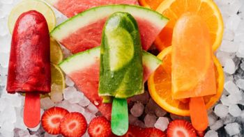 high angle view of some different homemade ice pops, made with different natural fruit juices and pieces of fruit, such as watermelon, strawberry, peach, lime or orange, placed on ice