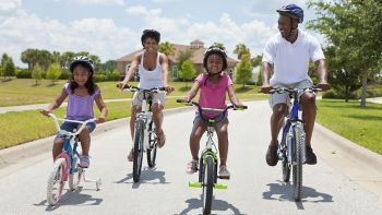 A Black African American family of two parents and two children, two girls, cycling together.