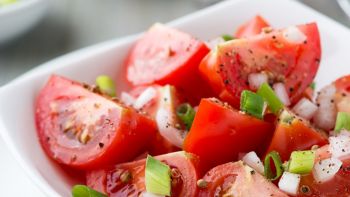 Tomato salad with spring onion and coriander seeds. Home made food. Symbolic image. Concept for a tasty and healthy meal. Bright wooden background. Close up