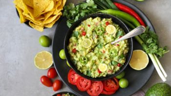 Delicious bowl of traditional   Mexican Guacamole, nachos and guacamole ingredients: Avocado, onion, cilantro, hot pepper tomatoes and lime.Top view, flat lay. Fresh, raw, vegetarian dish, copy space 