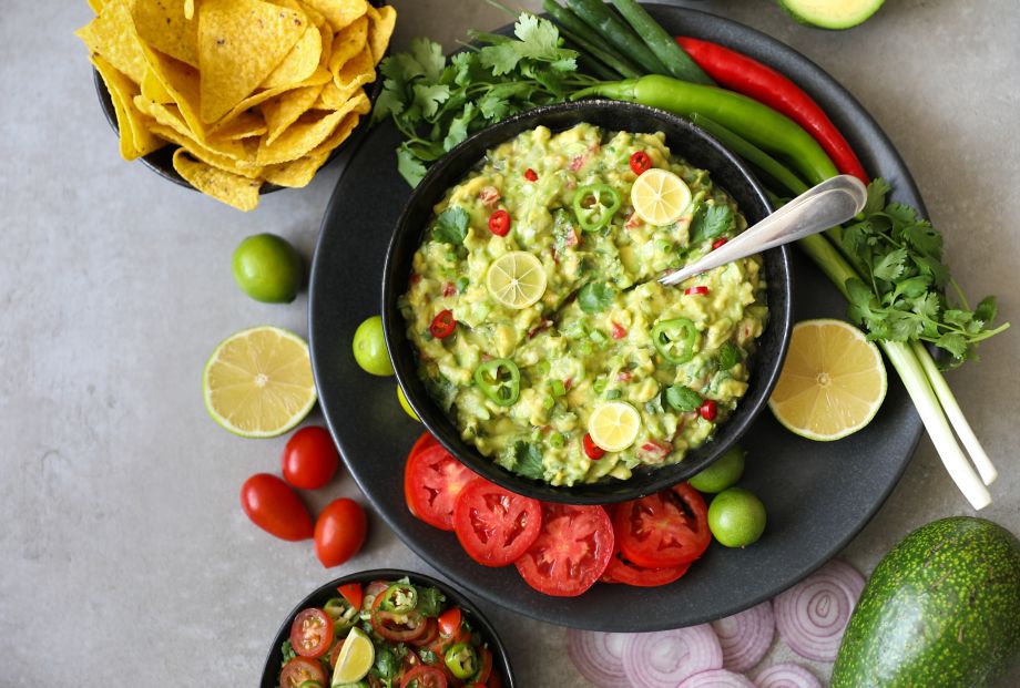 Delicious bowl of traditional   Mexican Guacamole, nachos and guacamole ingredients: Avocado, onion, cilantro, hot pepper tomatoes and lime.Top view, flat lay. Fresh, raw, vegetarian dish, copy space 