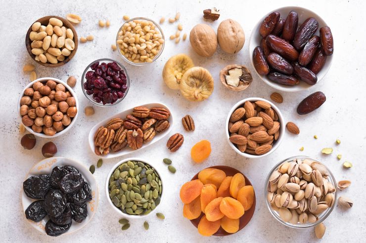 Dried fruits and Nuts in bowls on white background, top view, copy space. Healthy snack - assortment of organic dry fruits and various nuts.