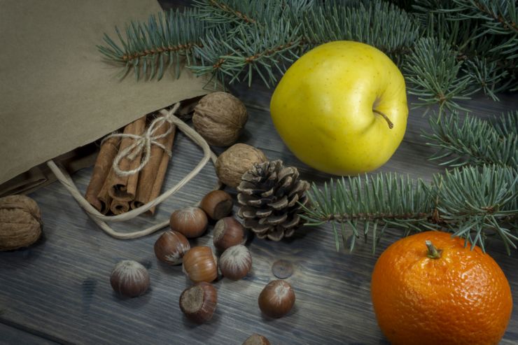 Various nuts, cinnamon yellow apple and clementine as concept of holiday groceries, spread on wooden table out of paper shopping bag, viewed in close-up from high angle with fir tree branch