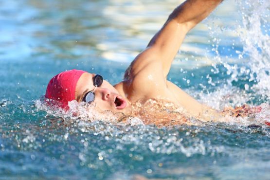 Man swimming crawl in blue water. Portrait of an athletic young male triathlete swimming crawl wearing a pink cap and swimming goggles while. Triathlete training for triathlon.; Shutterstock ID 142342759; Purchase Order: Informed Choice Fact Sheet; Job: ; Client/Licensee: ; Other: 