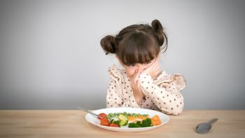 Nutrition & healthy eating habits for kids concept. Children do not like to eat vegetables. Little cute kid half race girl refuse to eat healthy vegetables.