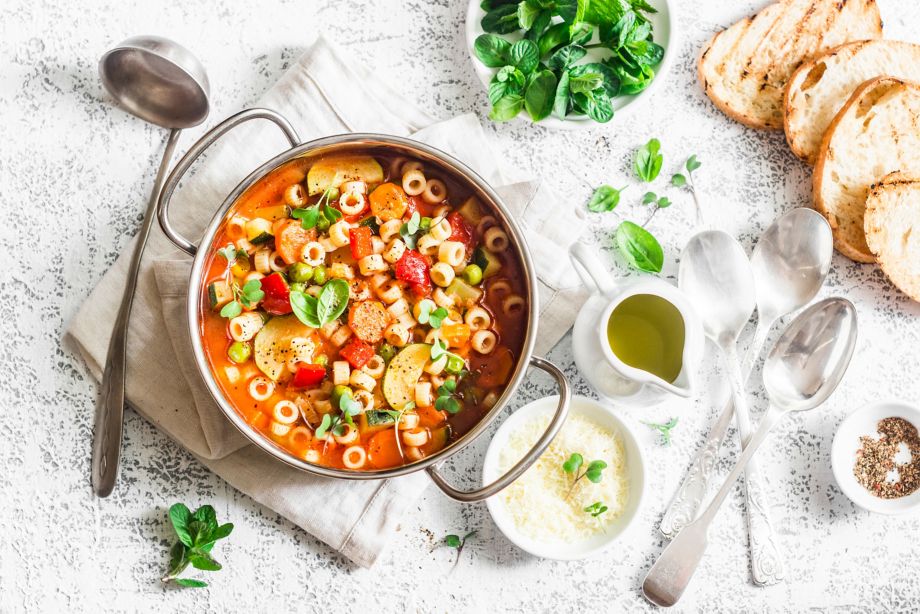 Minestrone soup in a pan on a light table, top view. Italian soup with pasta and seasonal vegetables. Delicious vegetarian food concept. Flat lay   