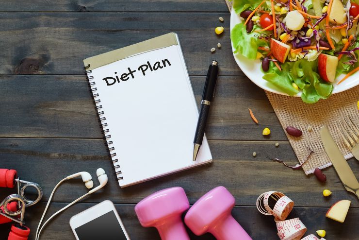 Top view on wooden table with Salad, dumbbells, measure tape, smartphone and  notebook with diet plan text. Diet, fitness and healthy eating with healthy recipes concept.  Copy space for text or your diet plan.