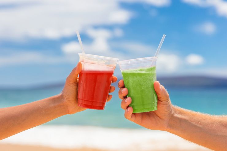 Healthy juice smoothie drinking couple toasting cold pressed organic drinks together at beach restaurant. Detox smoothie drink toast at summer vacations holidays. Fruit juicing weight loss diet.