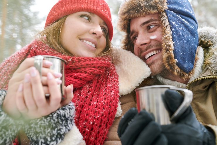 Head and shoulders portrait of loving young couple enjoying hot cocoa during date in beautiful winter forest and looking at each other tenderly