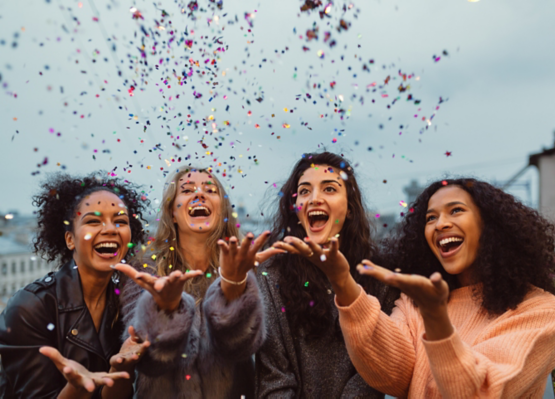 Happy friends standing on a terrace. Group of young women throwing confetti.